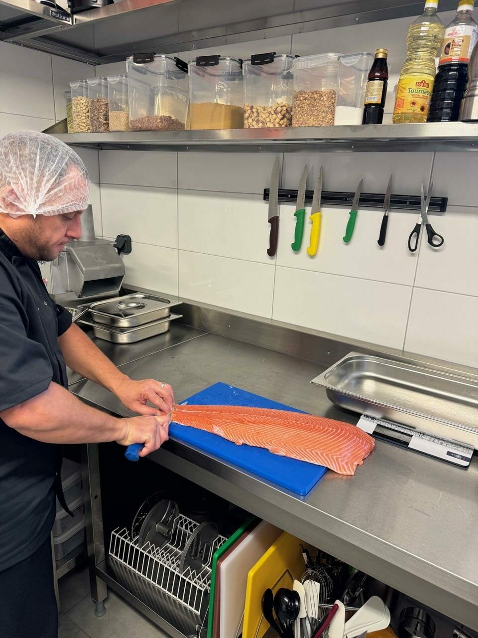 fraich-heure-preparation-poke-bowl-saumon-frais cuisinier-habillee-de-noir-levant-les-filets-de-saumon-frais-pour-poke-bowl-dans-cuisine-industrielle-avec gants-et-charlotte